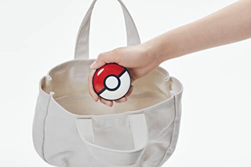 Hand houdt een Pokébal boven een tas.